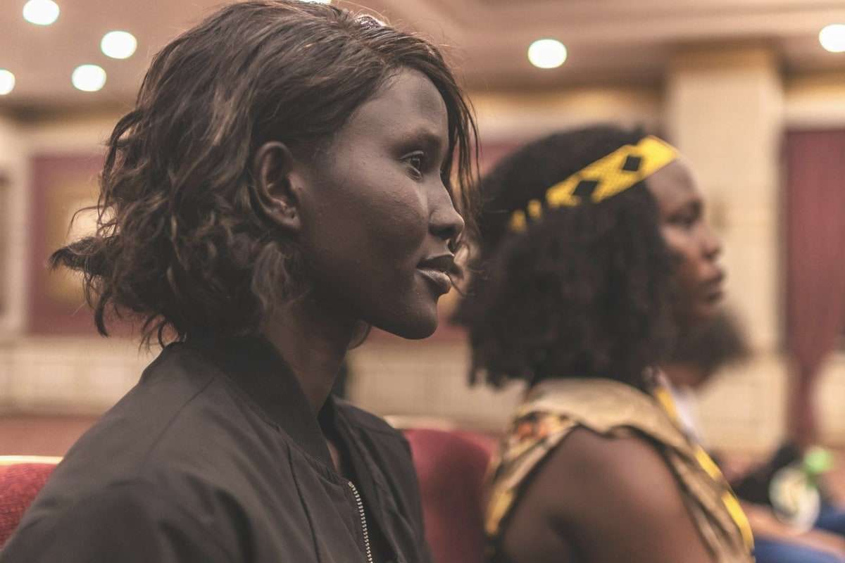 Two women seated side by side in profile, listening at an event.