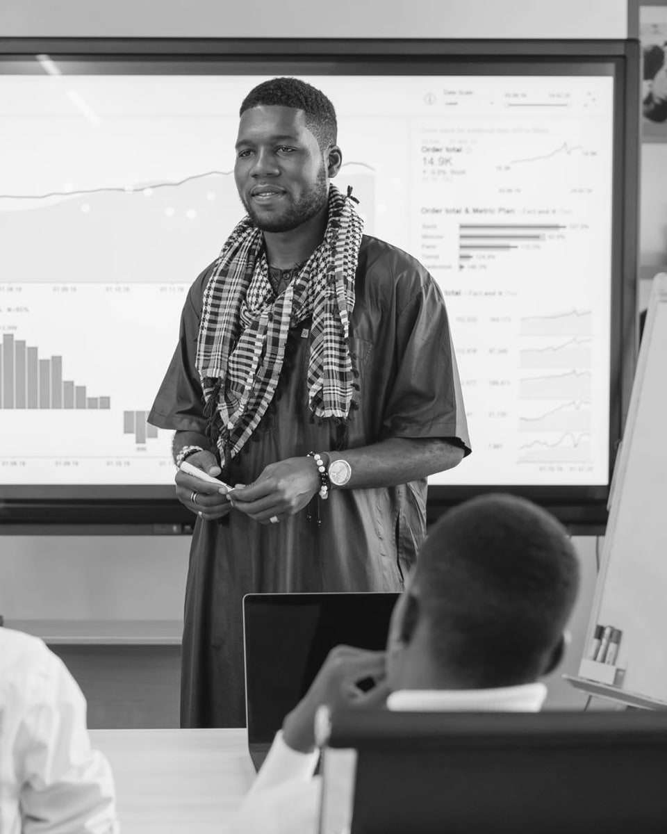 A man presenting charts on a wall screen to colleagues in a meeting room.